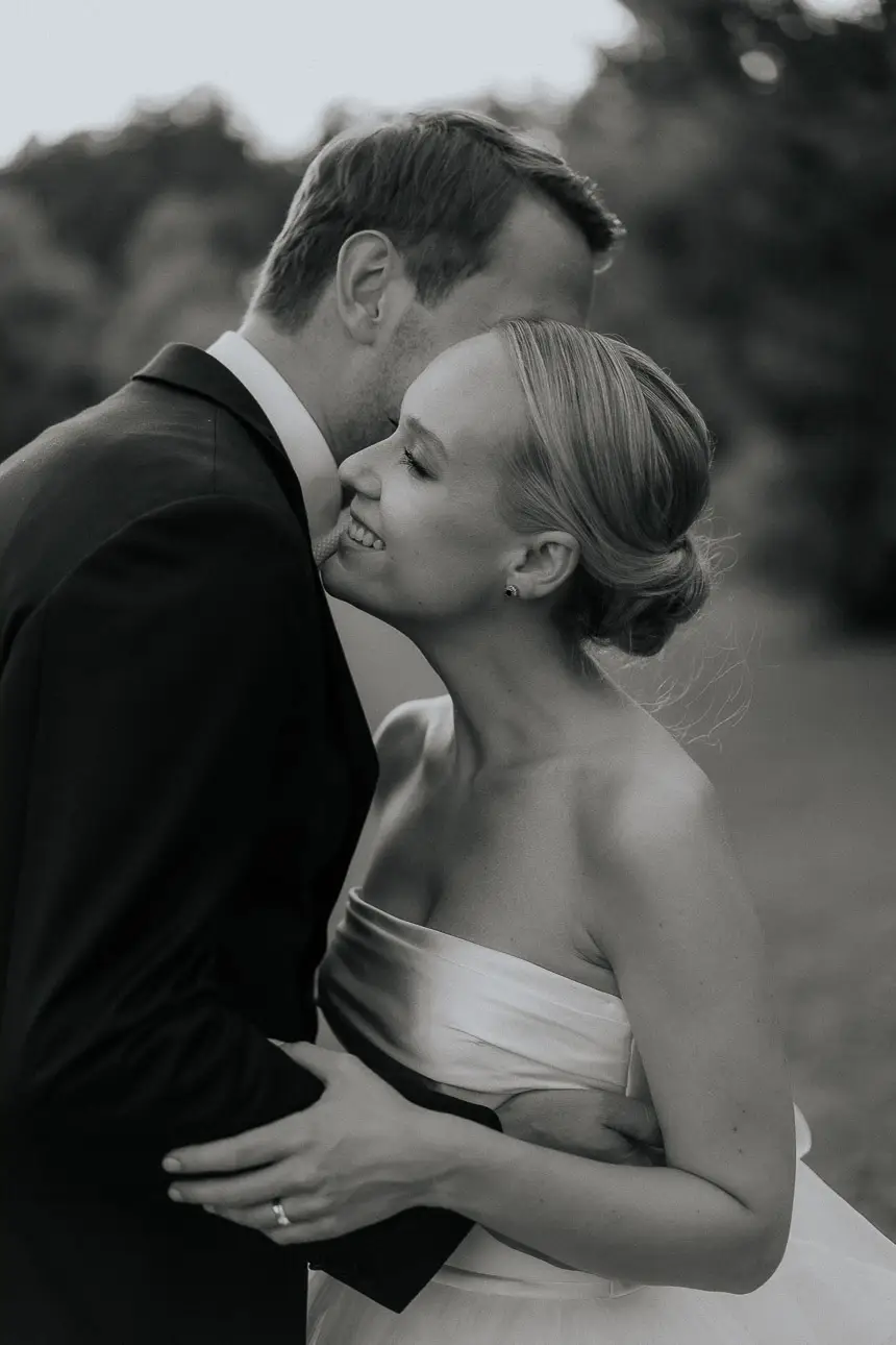 nahes schwarz weiß Foto eines verliebten, sich umarmenden und glücklichen Brautpaares am Tag Ihrer Hochzeit mit der Braut im Vordergrund